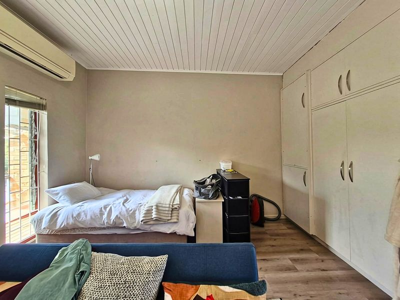 A bedroom featuring laminate flooring, a tongue and groove ceiling, built-in cupboards, and an air conditioning unit.
