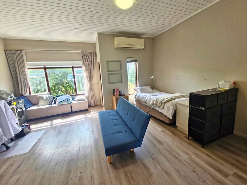 Spacious bedroom featuring laminate flooring, a split-system air conditioner, and large windows with security bars, offering a functional and well-lit living space.