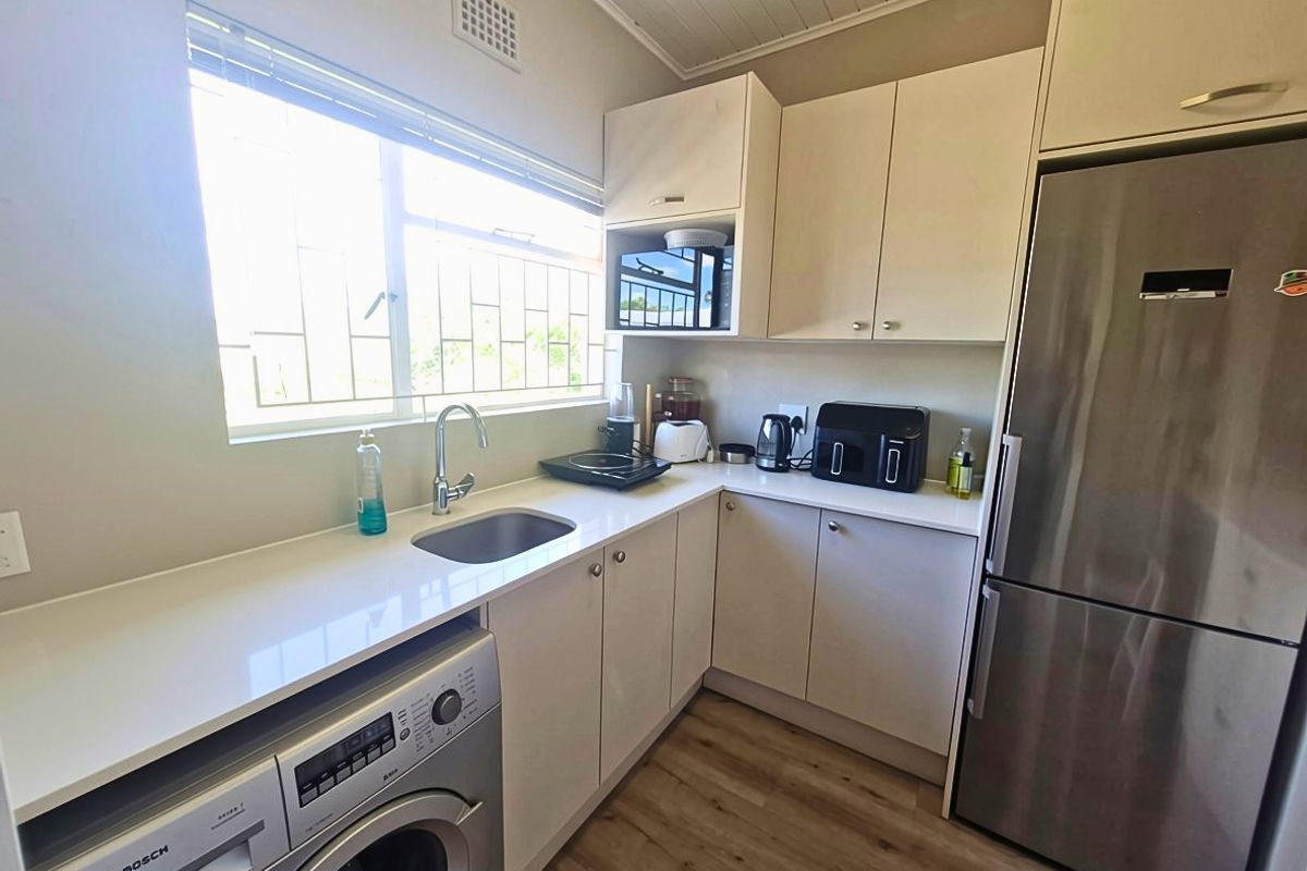 A compact, functional kitchen featuring modern cabinetry, laminate countertops, a stainless steel sink, and integrated laundry appliance with timber-look flooring.