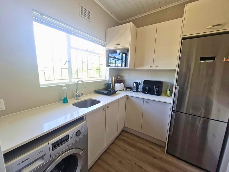 A compact, functional kitchen featuring modern cabinetry, laminate countertops, a stainless steel sink, and integrated laundry appliance with timber-look flooring.