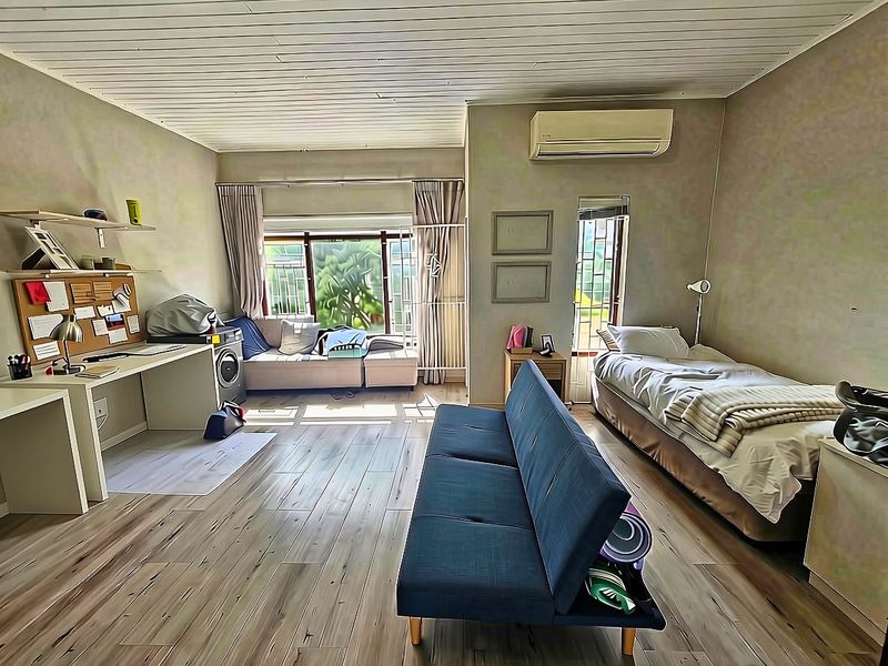 A bedroom featuring timber-look flooring, a built-in desk, and an air conditioning unit, with a timber-slat ceiling and natural light.