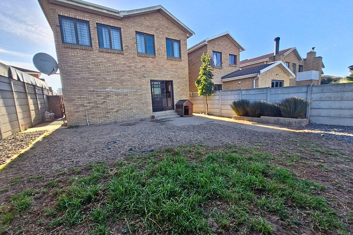 Rear view of a double-story face brick house featuring a private backyard with a precast concrete boundary wall and security gate access.