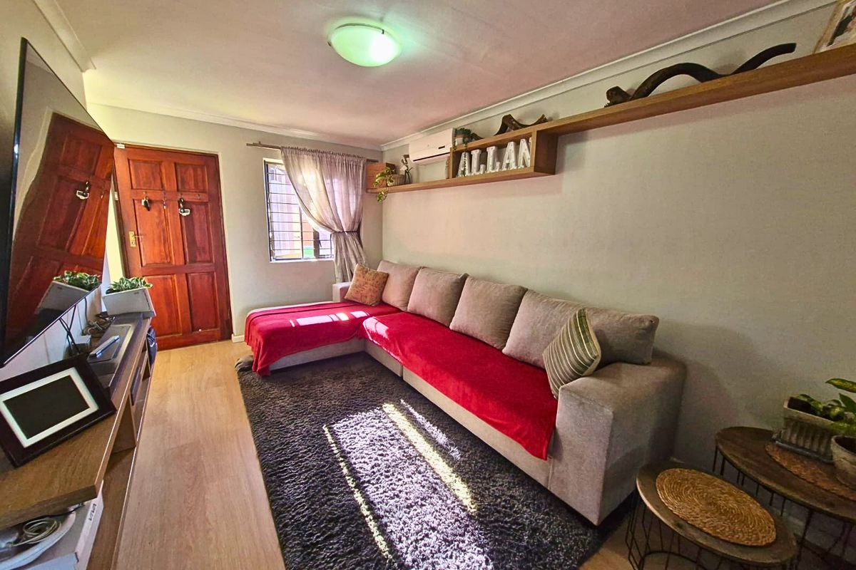 A cozy living room featuring laminate flooring, a split-system air conditioner, and a floating wall shelf, providing a functional and comfortable living space.