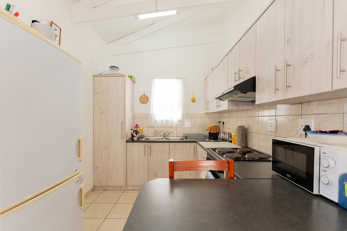 A functional kitchen featuring light wood-look cabinetry, dark countertops, a built-in electric hob with extractor, and a vaulted ceiling with tiled flooring.