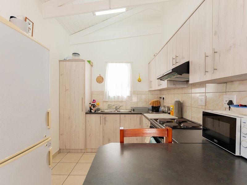 A functional kitchen featuring light wood-look cabinetry, dark countertops, a built-in electric hob with extractor, and a vaulted ceiling with tiled flooring.