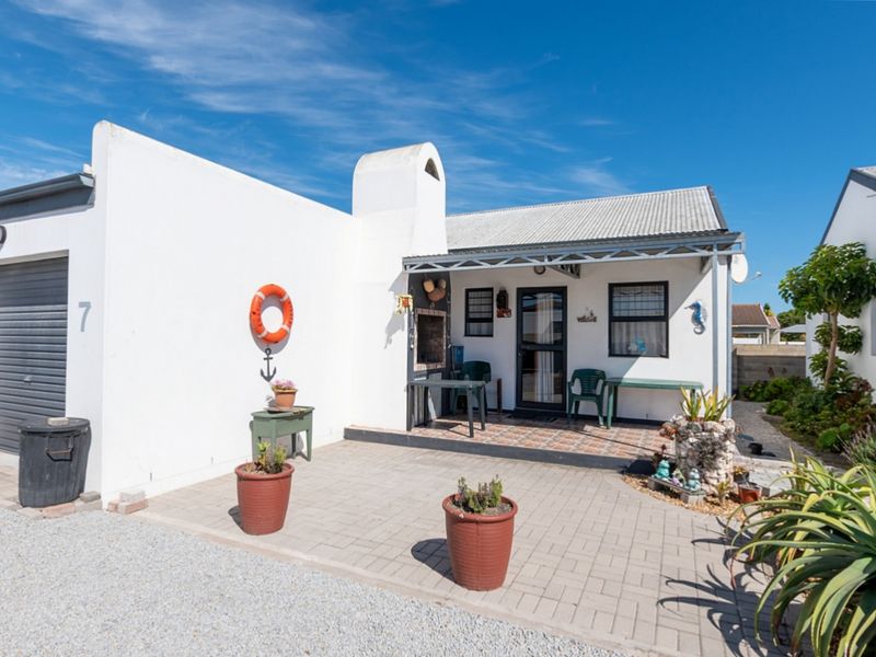 Front view of a coastal-style home featuring a paved driveway, integrated garage, and a covered patio area with a built-in braai.