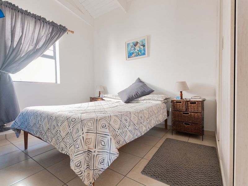 A bright bedroom featuring tiled flooring, a vaulted ceiling, and a built-in cupboard, offering a clean and functional living space.