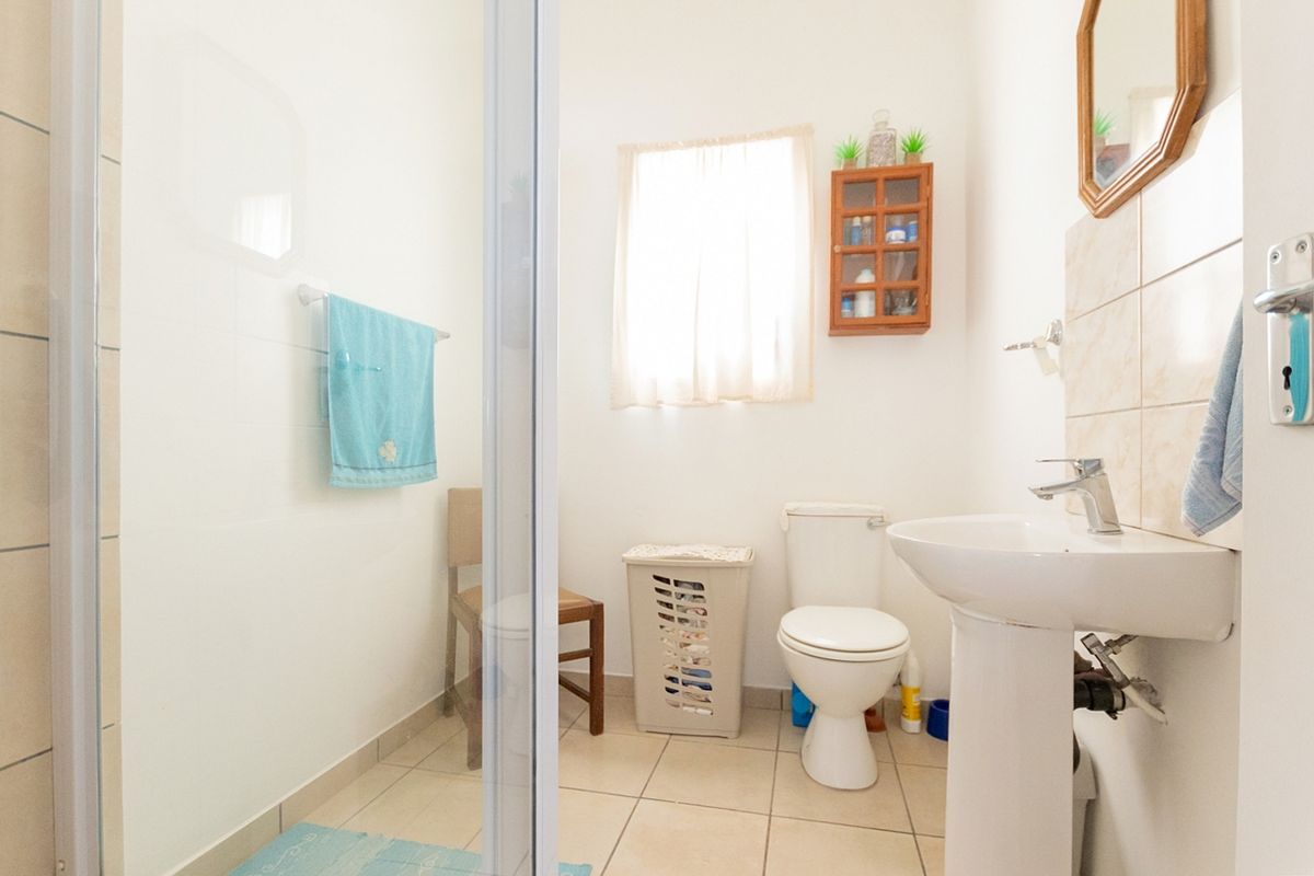 A functional bathroom featuring a pedestal sink, toilet, and a glass-enclosed shower with neutral wall and floor tiling.