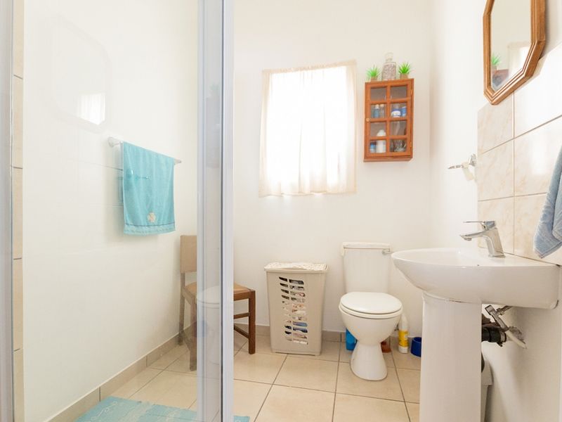 A functional bathroom featuring a pedestal sink, toilet, and a glass-enclosed shower with neutral wall and floor tiling.