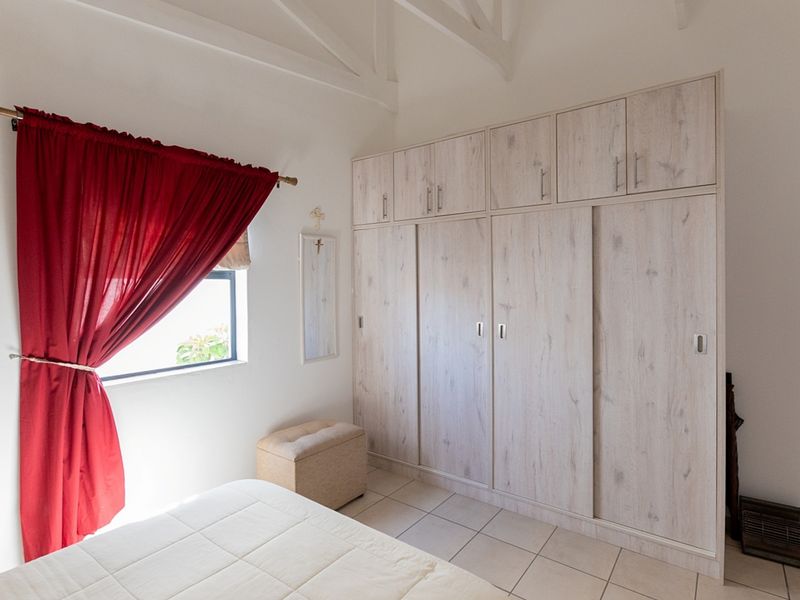 A well-lit bedroom featuring built-in cupboards with a light wood finish, tiled flooring, and exposed ceiling rafters.