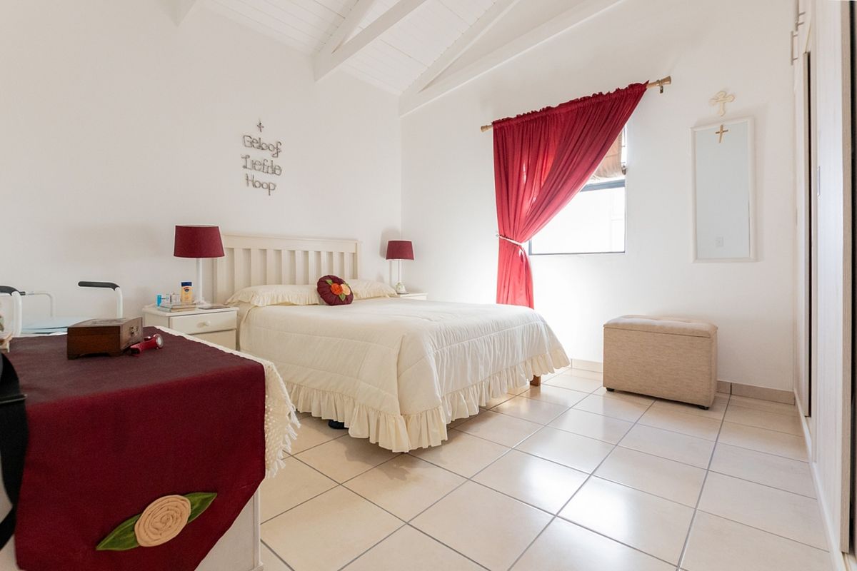 A bright bedroom featuring vaulted ceilings with exposed rafters, tiled flooring, and a built-in wardrobe, offering a clean and well-maintained living space.