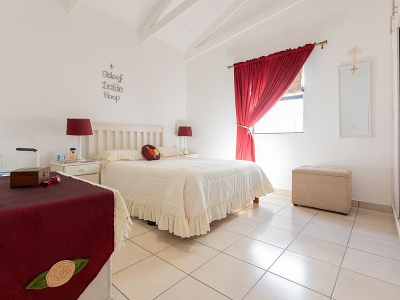 A bright bedroom featuring vaulted ceilings with exposed rafters, tiled flooring, and a built-in wardrobe, offering a clean and well-maintained living space.