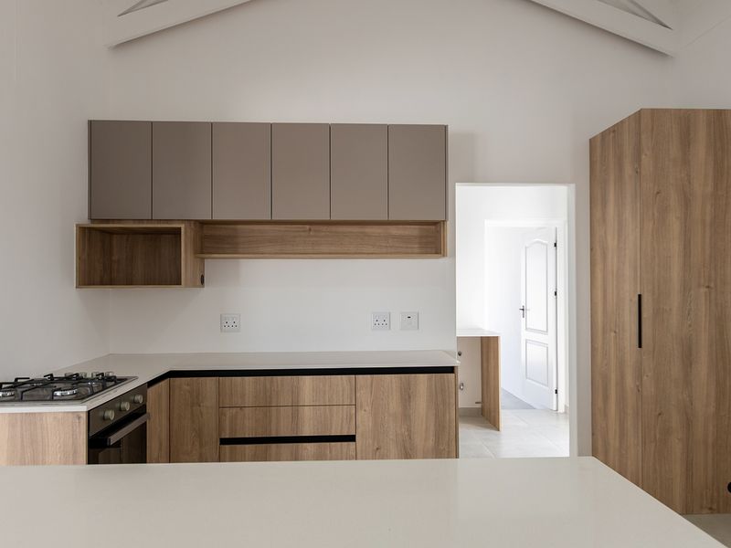 Modern kitchen featuring wood-grain cabinetry, stone countertops, integrated gas hob and oven, and a high vaulted ceiling, presenting a clean and contemporary aesthetic.