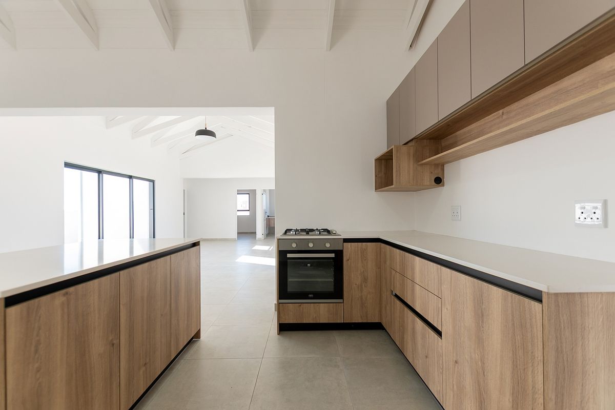 Modern kitchen featuring wood-grain cabinetry, stone countertops, built-in oven, gas hob, and exposed white timber ceiling beams in an open-plan layout.