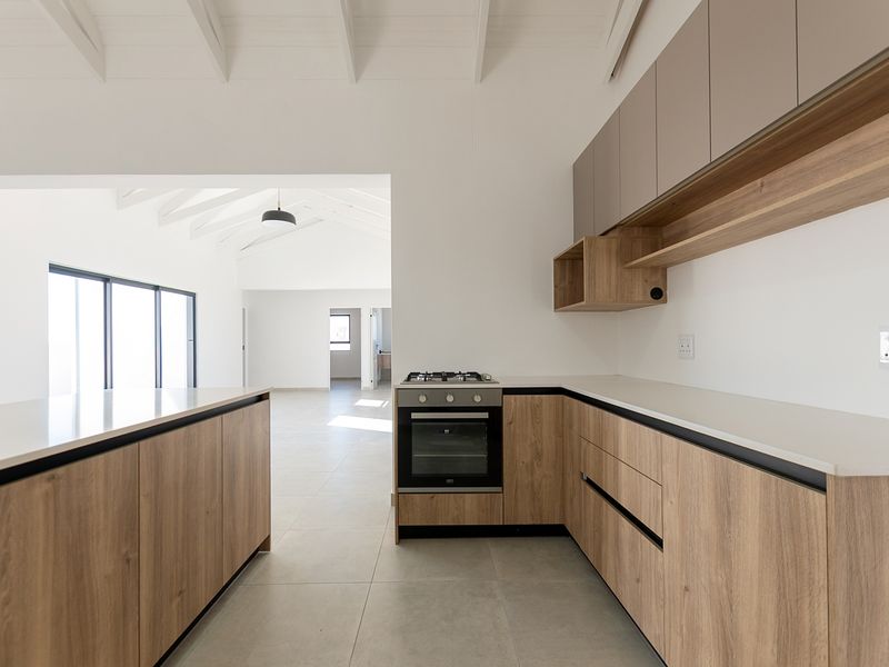 Modern kitchen featuring wood-grain cabinetry, stone countertops, built-in oven, gas hob, and exposed white timber ceiling beams in an open-plan layout.