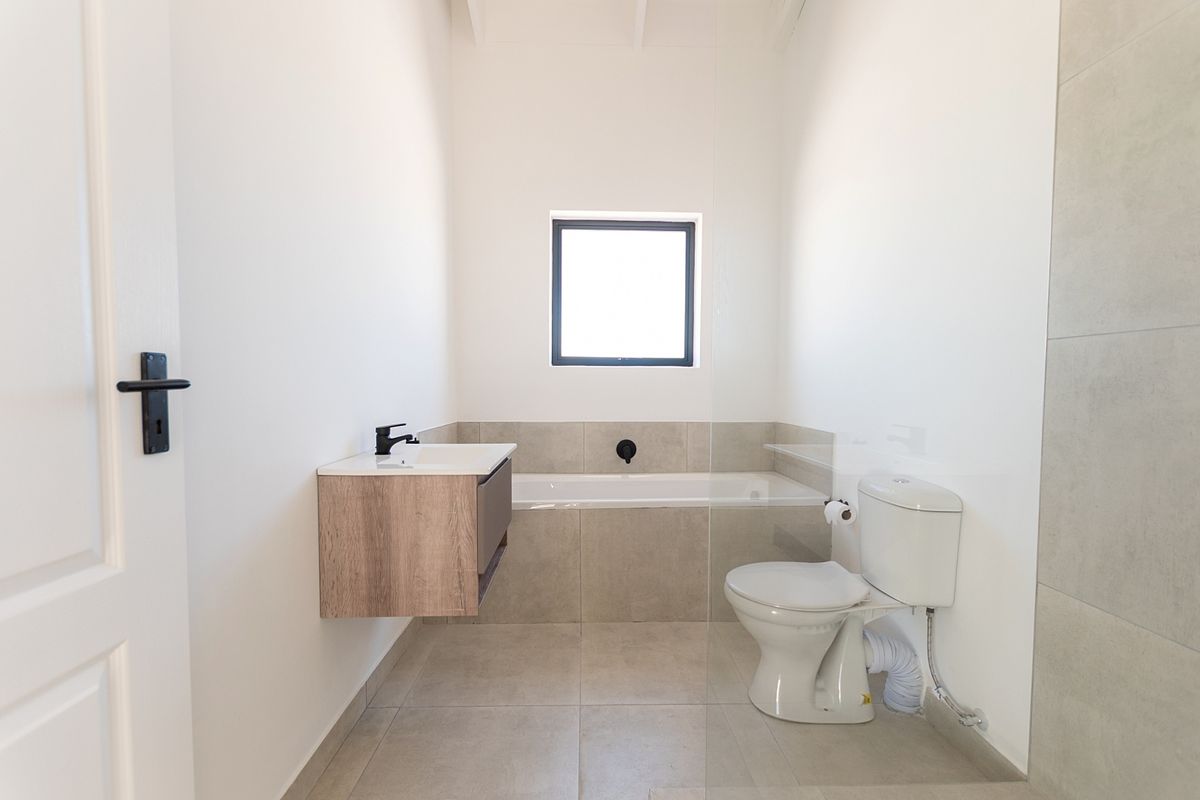 Modern bathroom featuring a wall-mounted vanity, built-in bathtub, and glass shower screen with neutral floor-to-ceiling tiling.