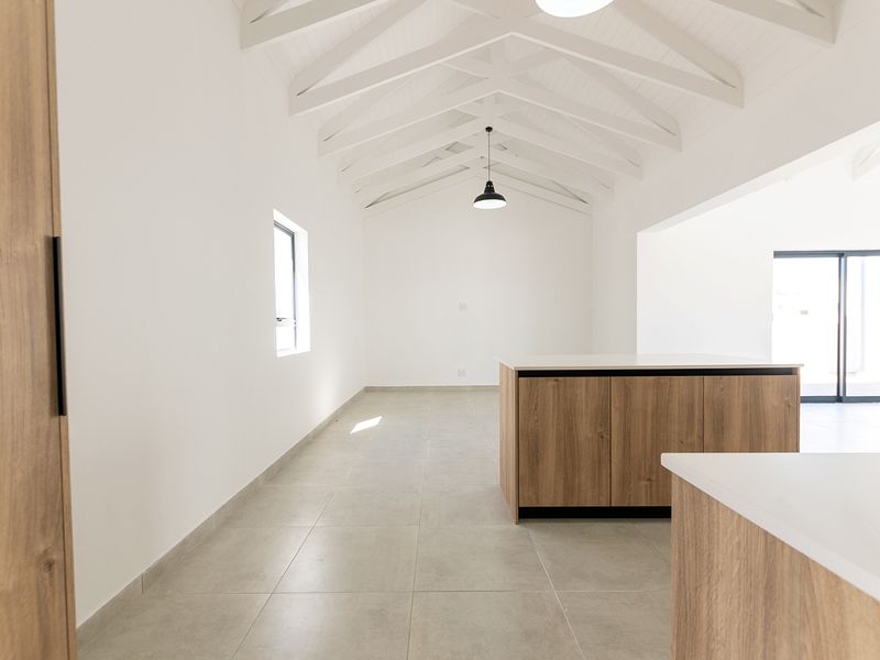 Modern, bright kitchen area featuring a central island, high vaulted ceilings with exposed white trusses, and large sliding doors leading to the exterior.
