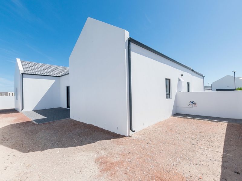 Rear view of a modern house featuring a paved patio area, white exterior walls, and a tiled roof with a surrounding boundary wall.