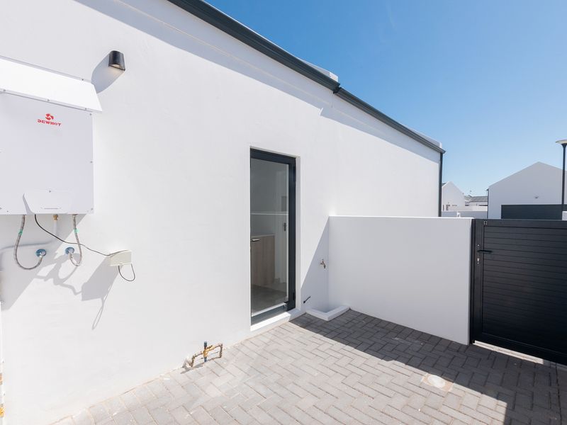 A clean, paved rear courtyard featuring a modern gas geyser, secure boundary wall, and a private pedestrian gate.