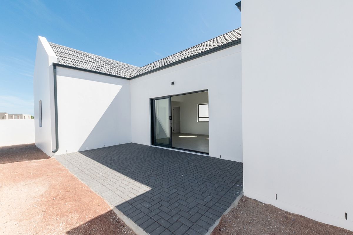 A modern rear exterior view featuring a paved patio area, sliding glass doors, and clean white rendered walls under a tiled roof.