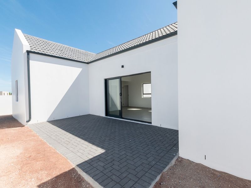 A modern rear exterior view featuring a paved patio area, sliding glass doors, and clean white rendered walls under a tiled roof.
