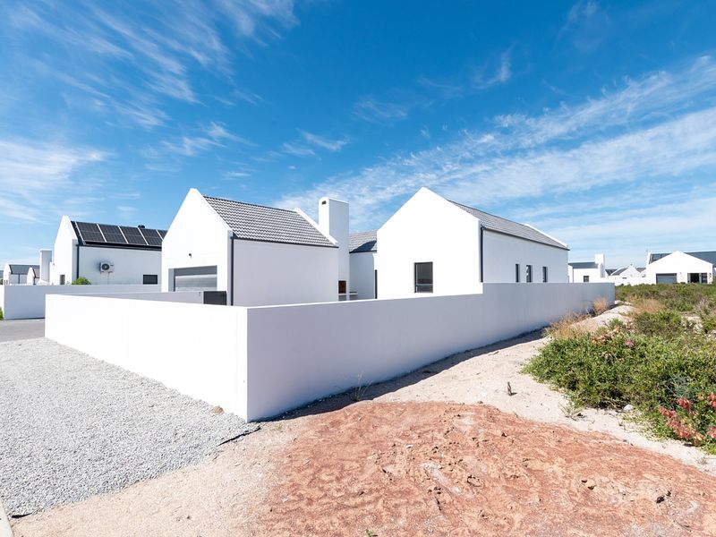 Modern white house exterior featuring a tiled roof, solar panels, and a clean perimeter wall in a well-maintained residential estate.