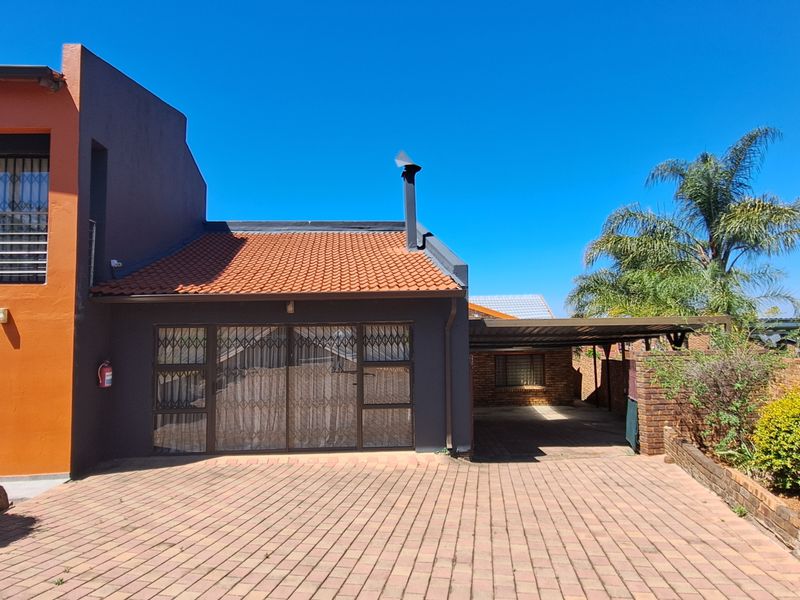 Front exterior view of the cottage featuring a paved driveway, carport, and terracotta roof tiles with secure metal gate access.