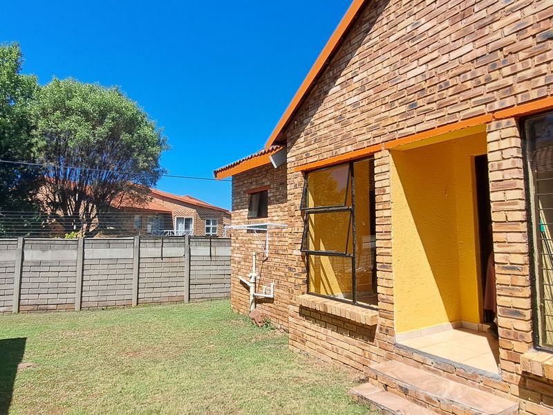 Rear view of the cottage featuring face brick construction, steel-framed windows with security bars, and a private garden area enclosed by a concrete boundary wall.