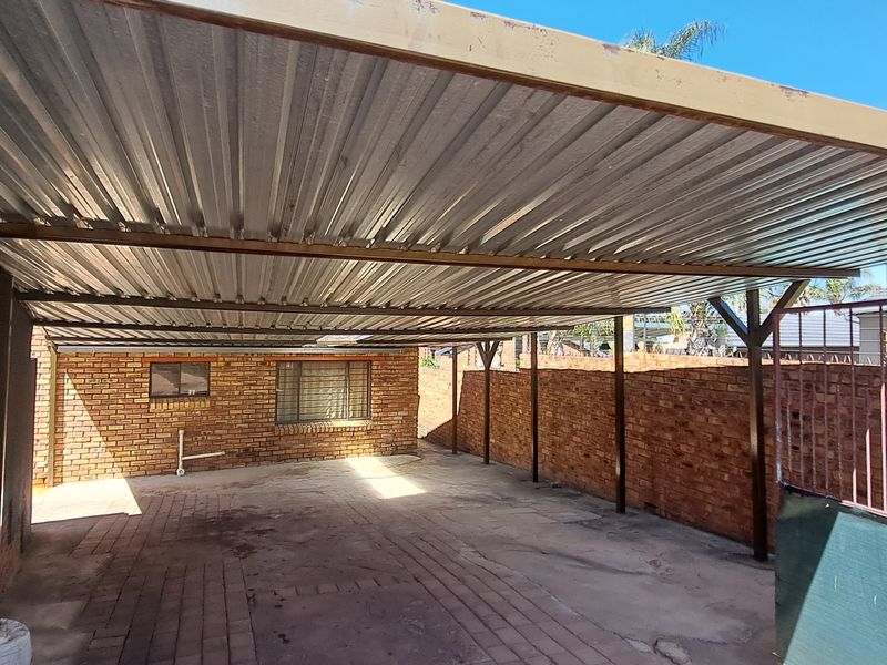 A spacious covered carport area featuring a corrugated metal roof, brick boundary walls, and paved flooring, providing secure off-street parking.