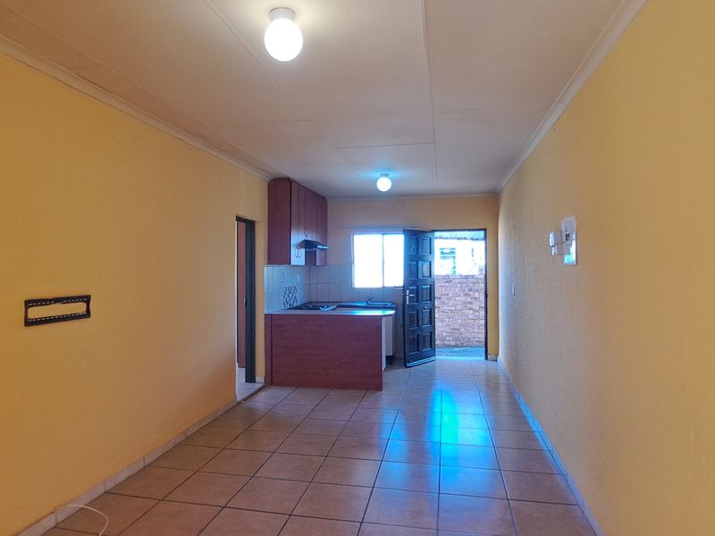 An open-plan living and kitchen area featuring tiled flooring, dated cabinetry, and direct access to the exterior.