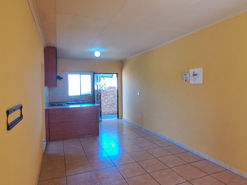 An open-plan living and kitchen area featuring tiled flooring, built-in cabinetry, and a functional kitchen layout with direct access to the exterior.