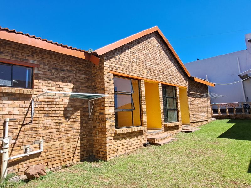 Rear view of a face brick cottage featuring a tiled roof, aluminium window frames, and a small private garden area.
