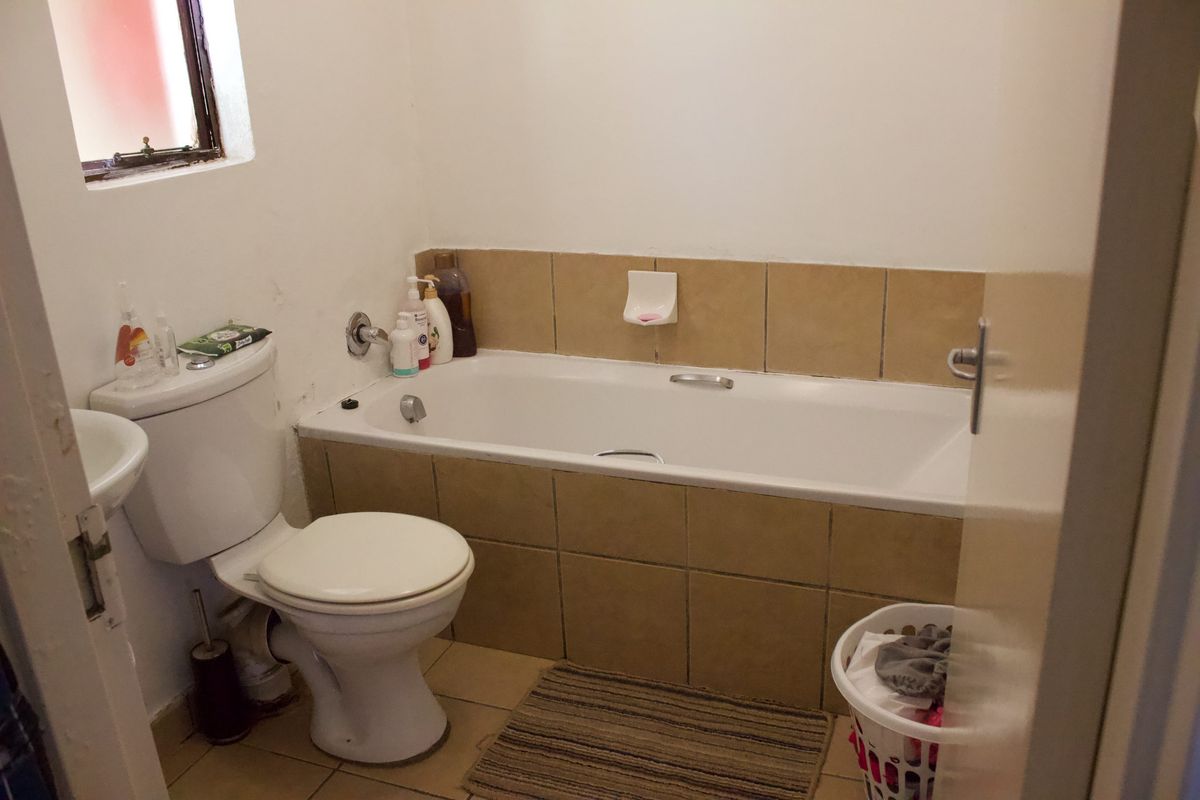 A functional bathroom featuring a bathtub with tiled surround, a standard toilet, and a pedestal basin with neutral floor tiling.