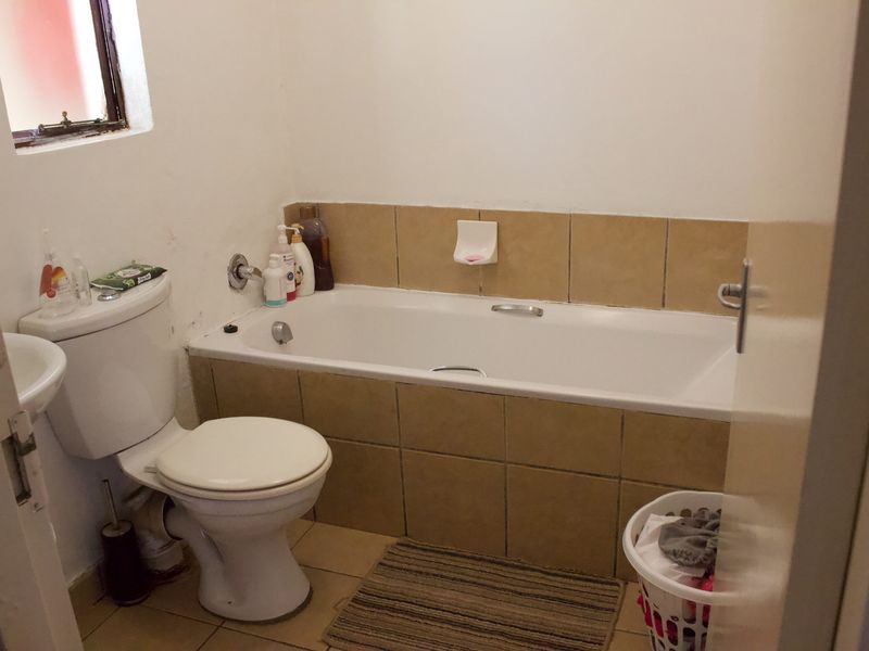 A functional bathroom featuring a bathtub with tiled surround, a standard toilet, and a pedestal basin with neutral floor tiling.