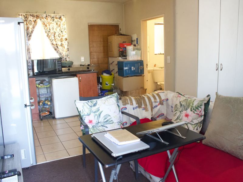 Open plan living area featuring a compact kitchen space with built-in cabinetry and tiled flooring, adjacent to a living area with built-in storage.