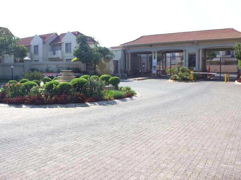 The entrance to Ibis Estate featuring a paved driveway, landscaped garden with a central water feature, and a secure gated access point.