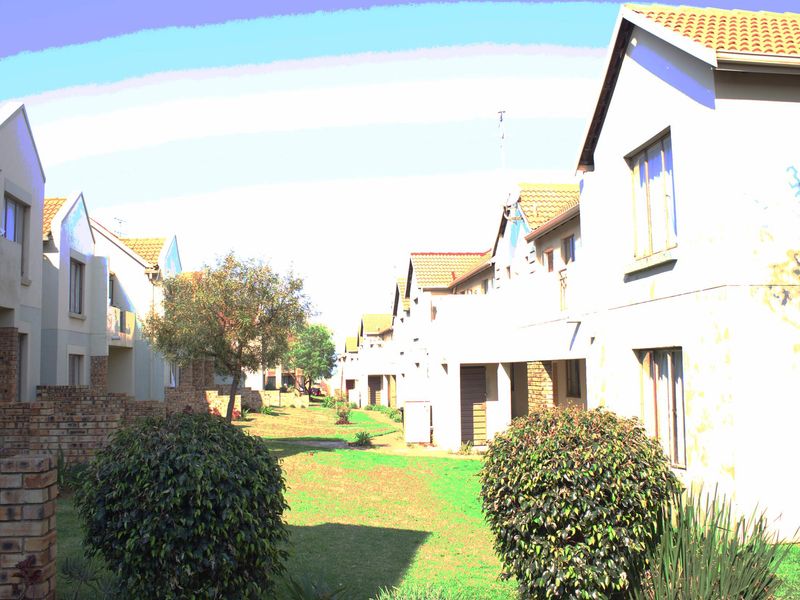 A view of the apartment complex exterior featuring brick facades, tiled roofs, and a shared communal garden area between the residential units.
