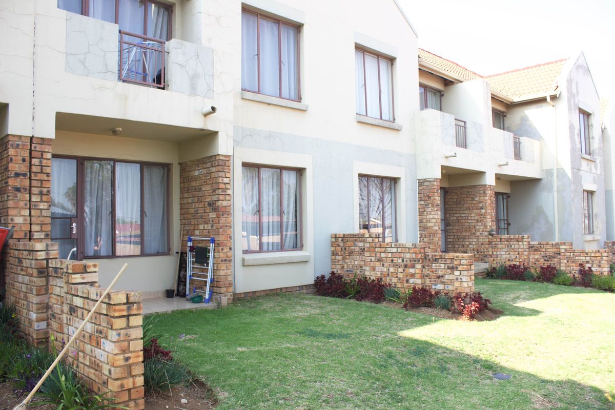 Rear view of a multi-story apartment complex featuring brick and plaster facades, private ground-floor patios, and shared garden spaces.