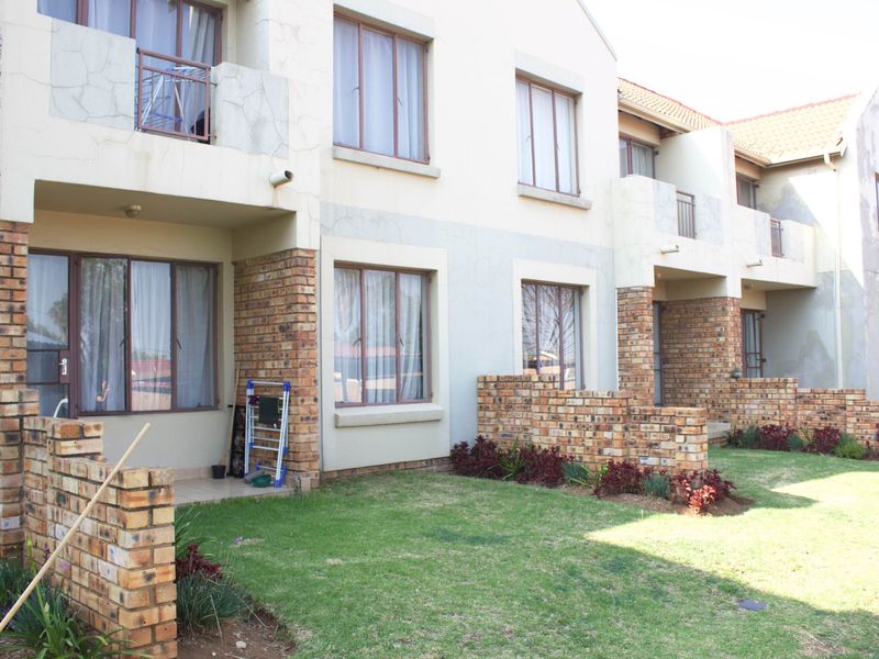 Rear view of a multi-story apartment complex featuring brick and plaster facades, private ground-floor patios, and shared garden spaces.