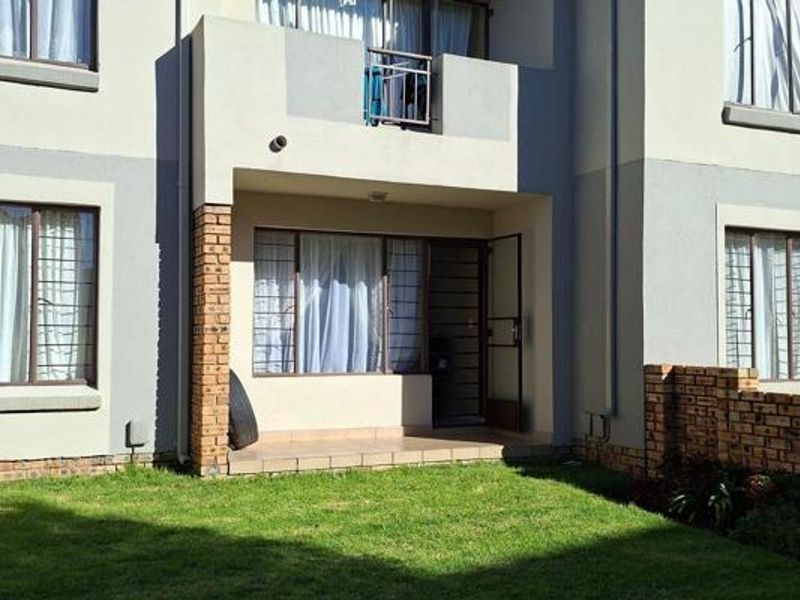 Rear view of the apartment building featuring a ground-floor tiled patio, a small private lawn, and an upper-level balcony with metal railings.