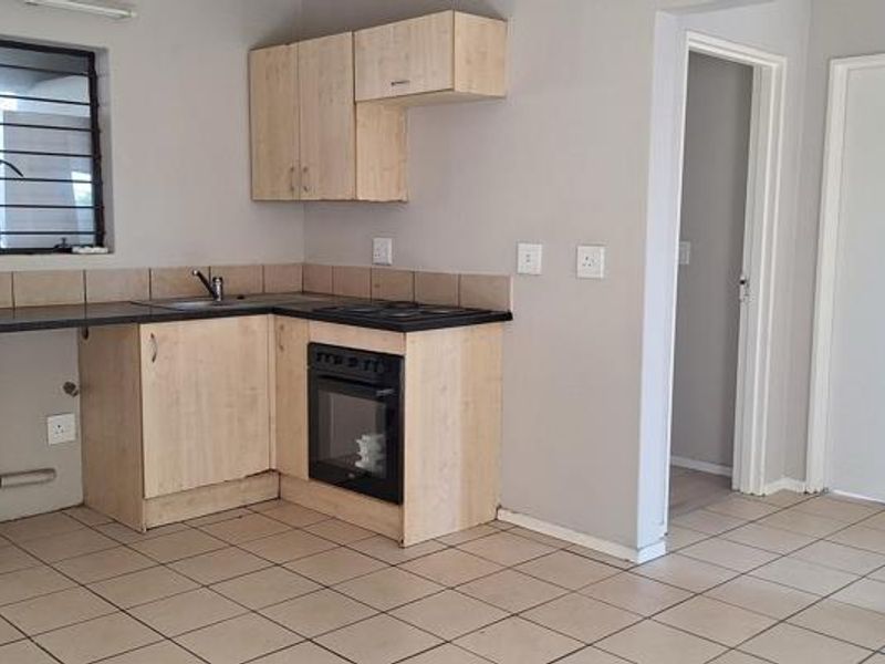 A functional kitchen featuring light wood-finish cabinetry, built-in oven and hob, tiled backsplash, and tiled flooring, offering a clean and practical workspace.