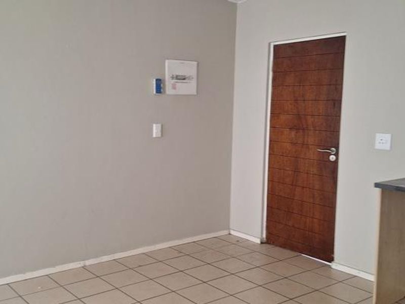 An empty open-plan living area featuring neutral wall tones, tiled flooring, and a solid wooden door, providing a blank canvas for interior design.