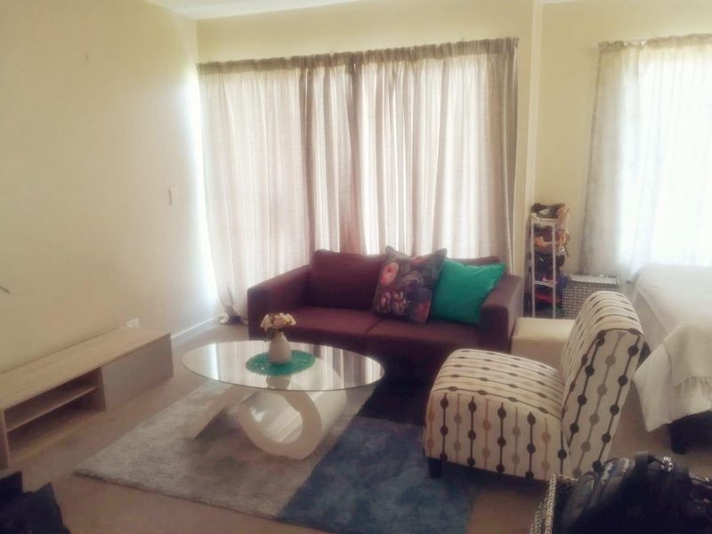A living room area featuring laminate flooring and large windows covered by curtains, providing a functional space for relaxation.