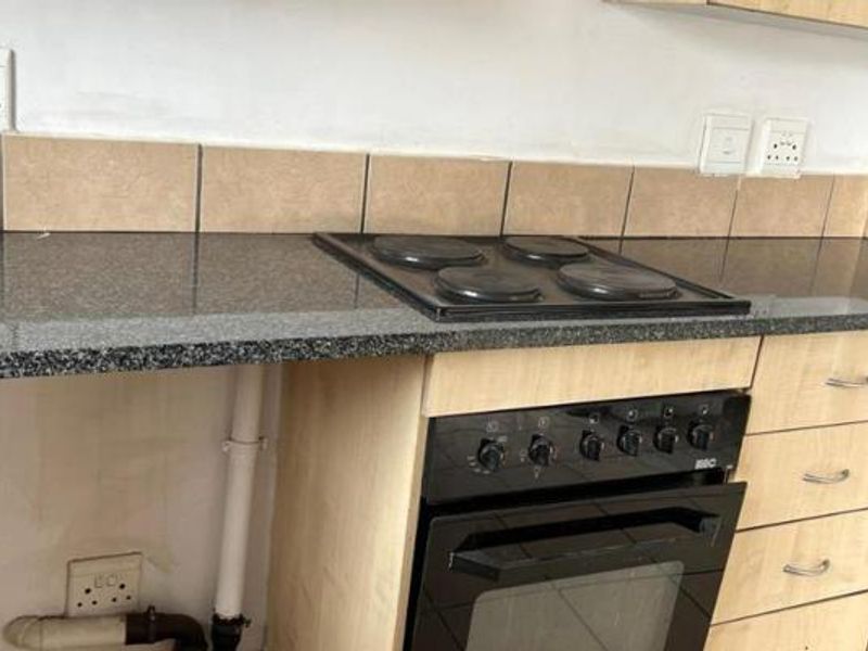 A kitchen area featuring a granite countertop, built-in oven, and electric hob, with visible exposed plumbing and unfinished wall sections requiring attention.