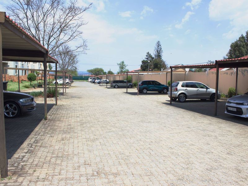 Outdoor parking area featuring multiple covered carports with paved surfacing and perimeter boundary walls.