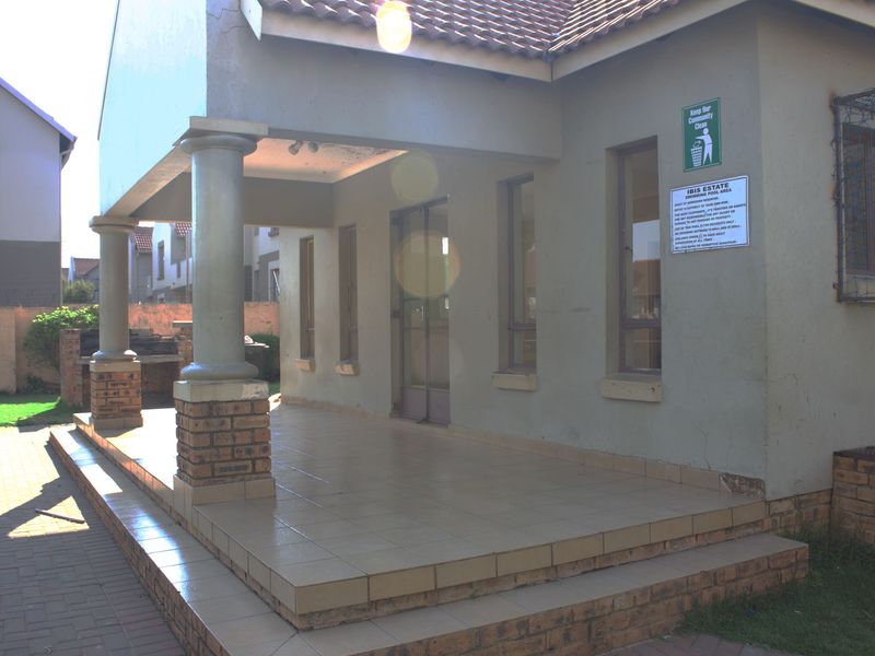 Exterior view of a communal pool area featuring a covered tiled patio, brick columns, and a built-in braai facility.
