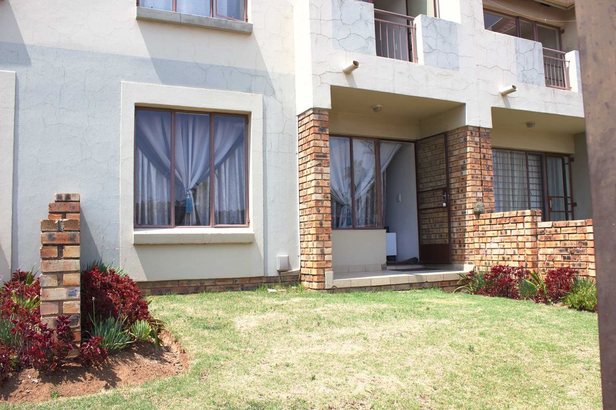 Rear view of the apartment featuring a small patio, face brick accents, and a private garden area with established landscaping.