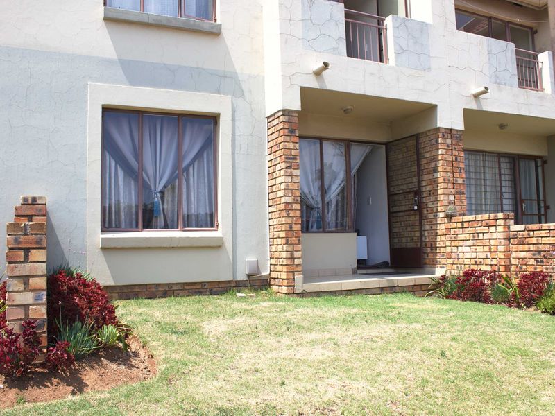 Rear view of the apartment featuring a small patio, face brick accents, and a private garden area with established landscaping.