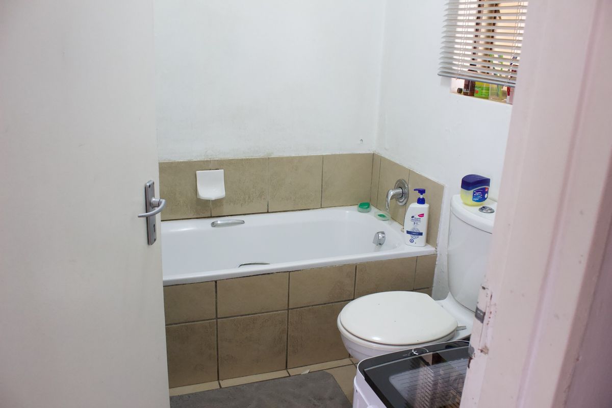 A compact bathroom featuring a standard bathtub with tiled splashback and a toilet, requiring some cosmetic updates to improve its overall condition.
