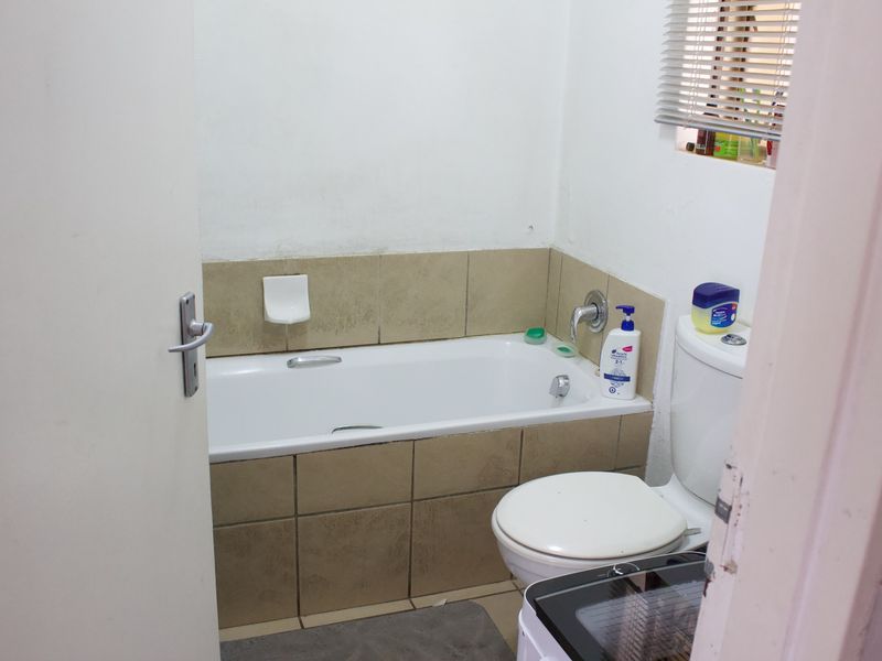 A compact bathroom featuring a standard bathtub with tiled splashback and a toilet, requiring some cosmetic updates to improve its overall condition.